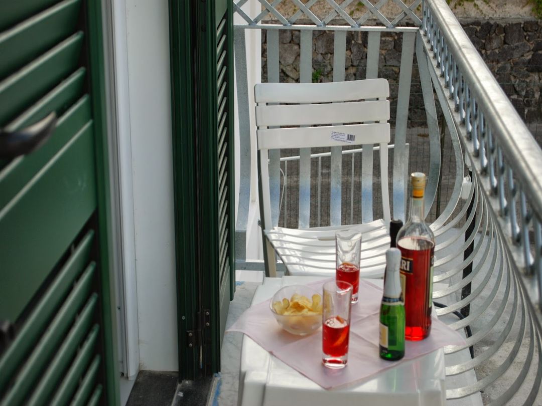 A balcony or terrace setup with white chairs, beverages, and snacks arranged on a pink table with metal railings visible.
