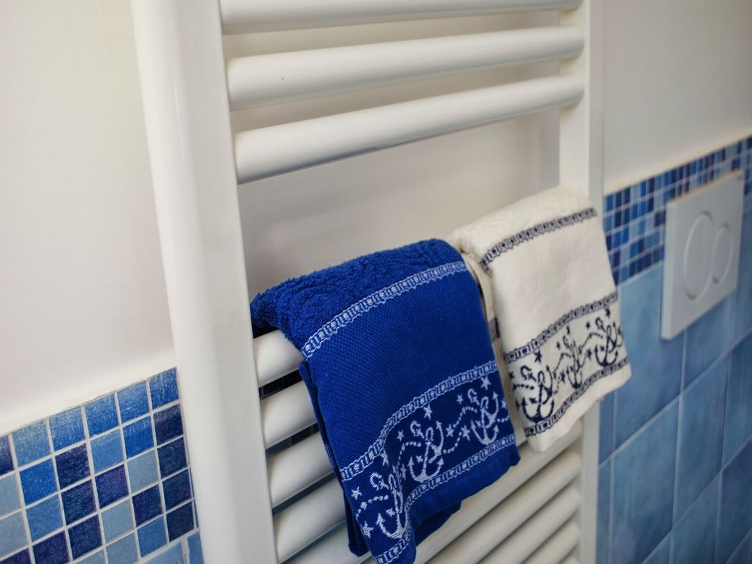 A white heated towel rack with blue and white decorative towels hanging in a bathroom with blue tile accents.