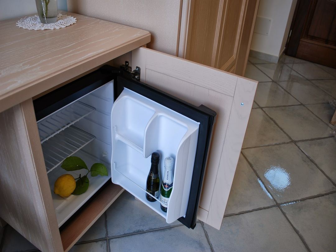 A small built-in refrigerator stocked with beverages and fresh lemons in a hotel room.